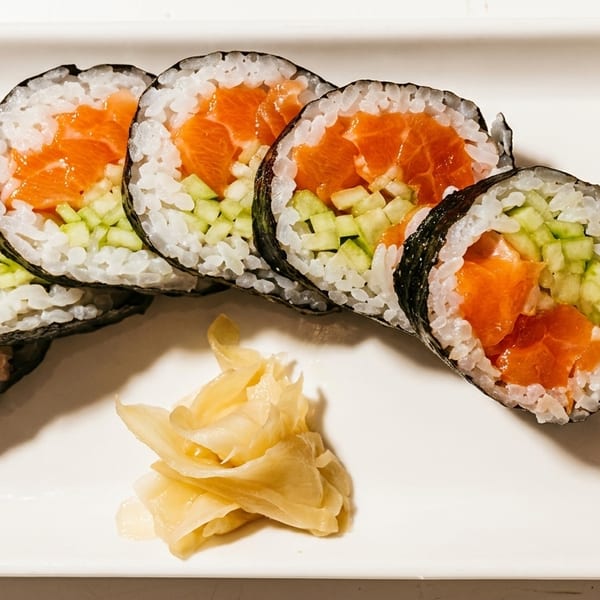 Salmon and cucumber sushi rolls with pickled ginger and wasabi on a white rectangular plate.