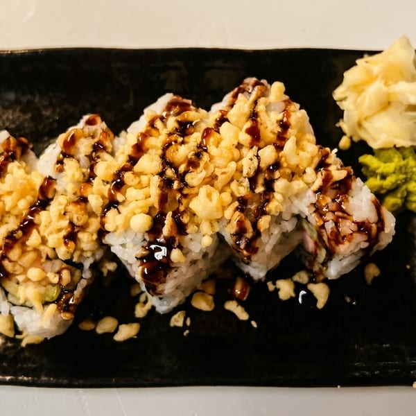 Sushi rolls topped with tempura flakes and dark sauce, served with ginger and wasabi.