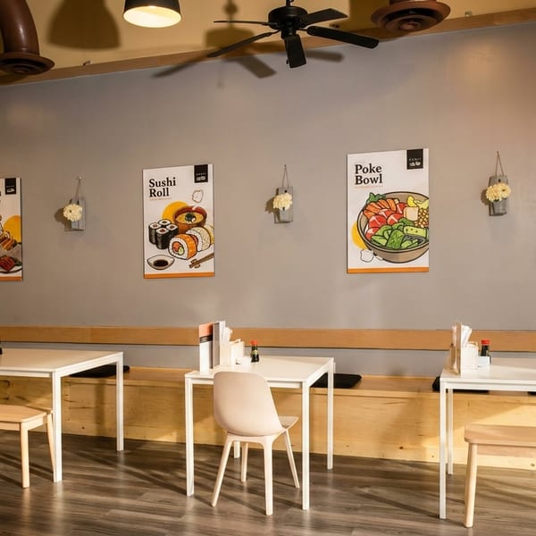 Interior of a modern restaurant with light wood tables, benches, and posters of sushi and poke bowls.