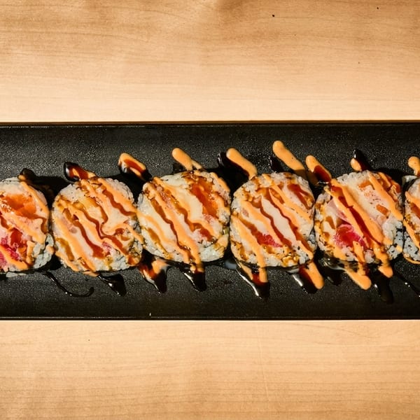 Six sushi rolls with orange and dark sauces, wasabi, and ginger on a black plate.