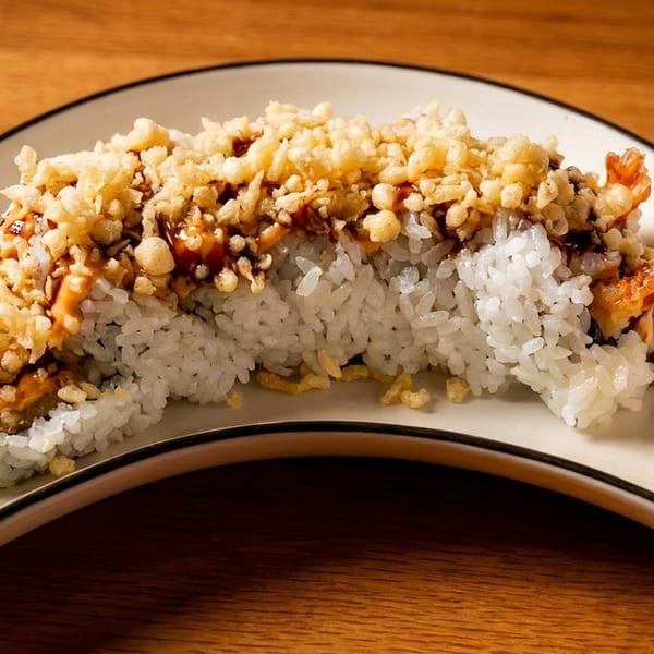 Sushi roll topped with crispy tempura flakes and sauce, served with wasabi and pickled ginger.