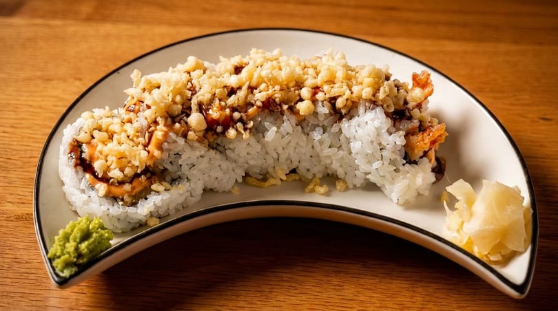 Sushi roll topped with crispy tempura flakes and sauce, served with wasabi and pickled ginger.