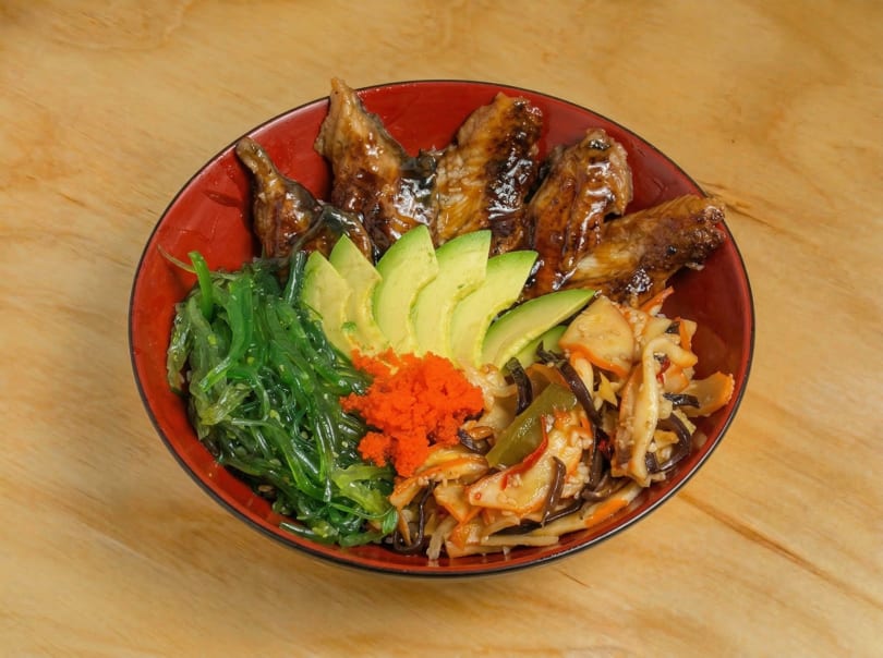 Red bowl filled with eel, avocado, seaweed salad, orange roe, and stir-fried vegetables.