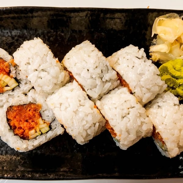 Spicy tuna sushi rolls with white rice, wasabi, and pickled ginger on a black plate.