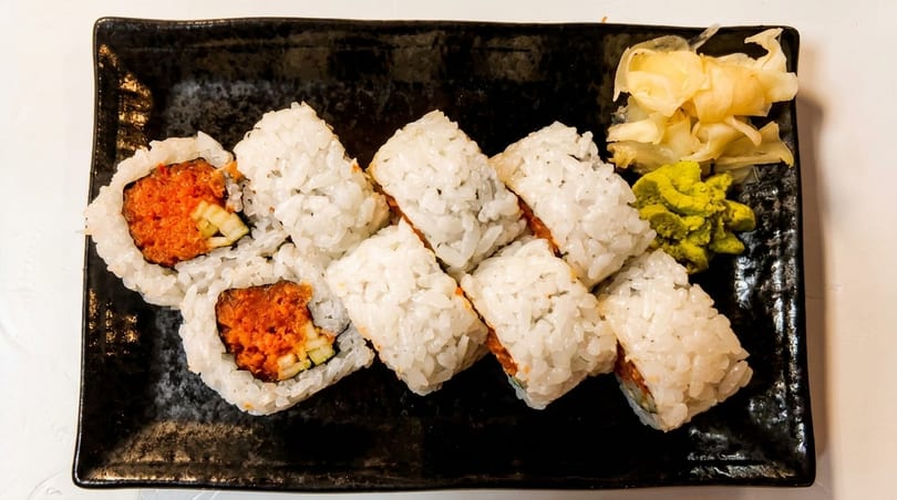 Spicy tuna sushi rolls with white rice, wasabi, and pickled ginger on a black plate.