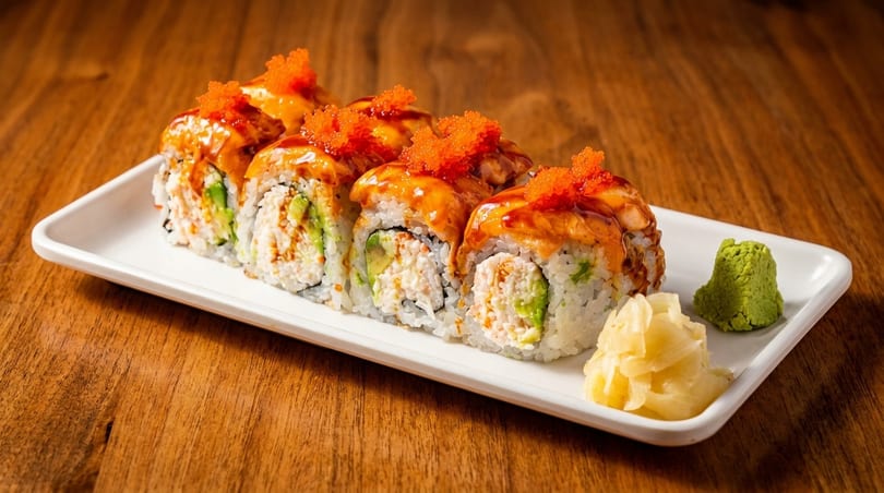Sushi rolls with avocado, crab, and roe on a white plate with wasabi and ginger.
