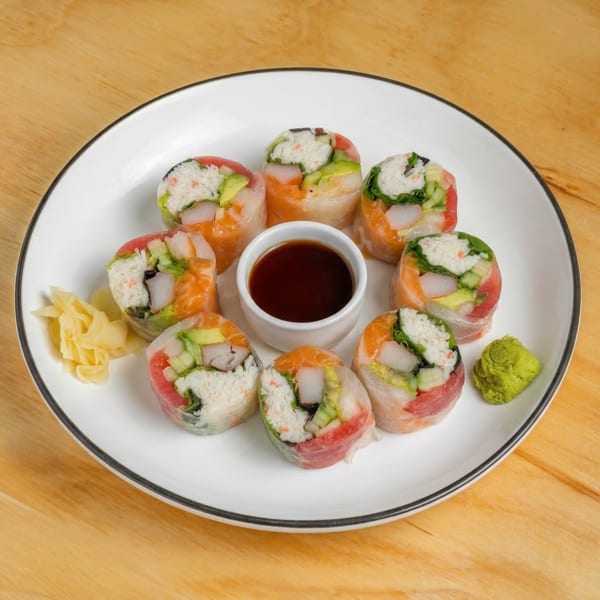 A white plate with eight colorful sushi spring rolls, soy sauce, pickled ginger, and wasabi.