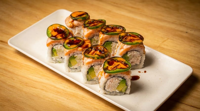 Sushi rolls with salmon, avocado, and jalapeño slices on a white rectangular plate.