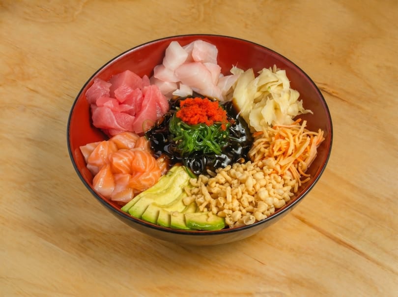 Colorful poke bowl with tuna, salmon, avocado, seaweed, roe, and crispy tempura bits.