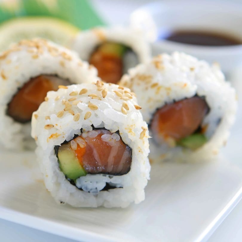 Sushi Go's salmon and avocado sushi rolls, topped with sesame seeds, on a white plate.
