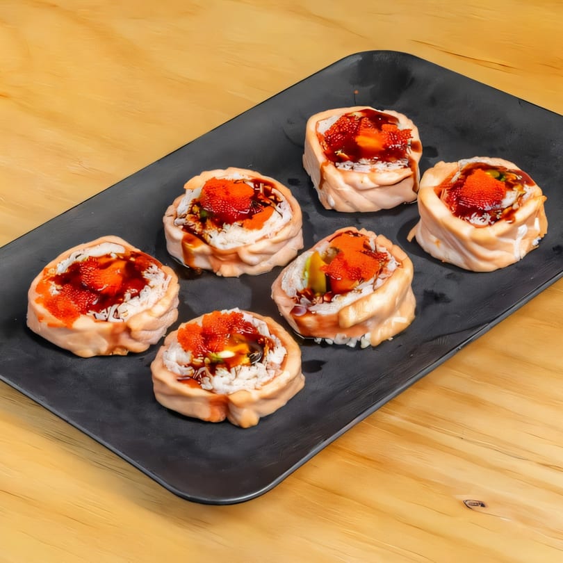Six salmon sushi rolls with orange roe and dark sauce on a black rectangular plate.